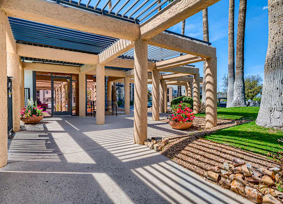 a covered walkway with trees and a building in the background