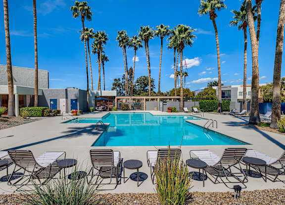 a swimming pool with chairs and tables and palm trees