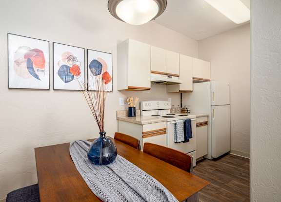 a dining room with a table and a kitchen with a white refrigerator