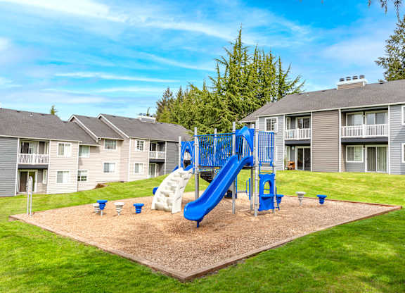 A playground with a blue slide and white slide in the middle of a sandy area.