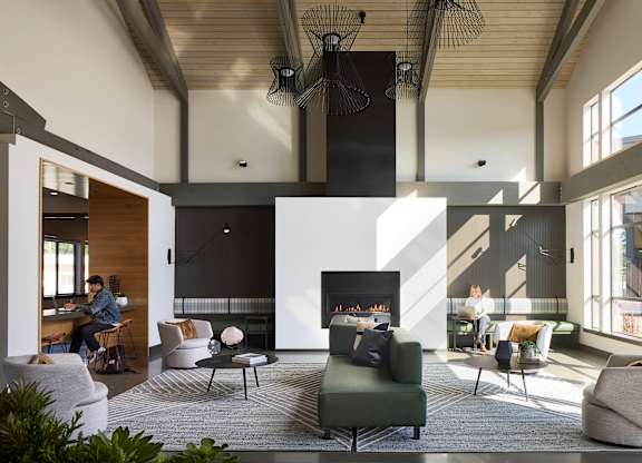a view of the living room with a fireplace and a woman sitting at a desk in the