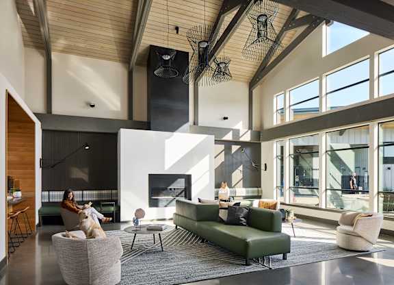 a woman sits on a couch in a large living room with a fireplace and large windows