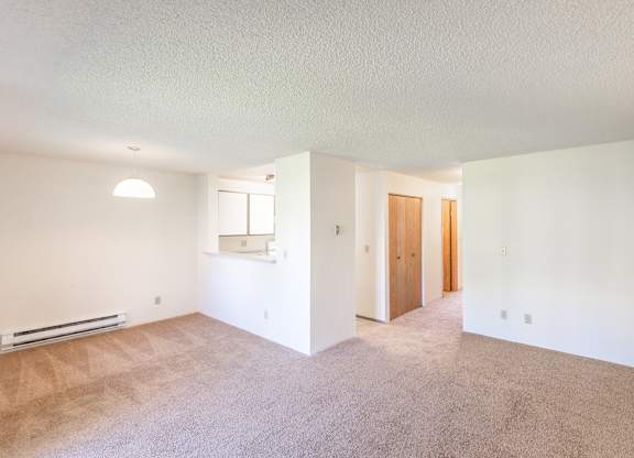 an empty living room with a kitchen in the background