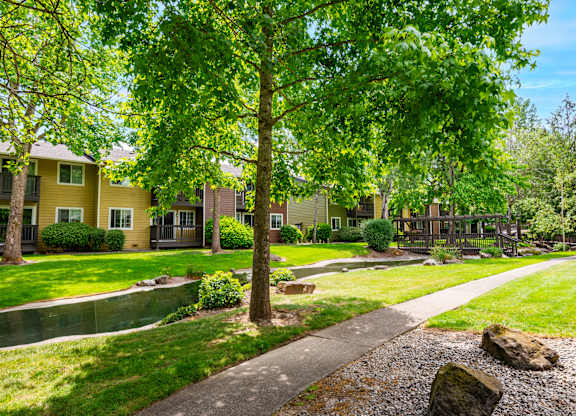 a pathway through the grassy area with trees and buildings in the background