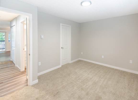 an empty living room with carpet and a door to a hallway