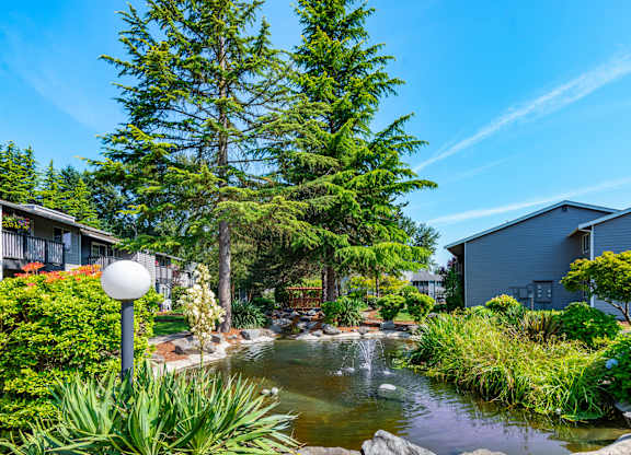 a garden with a pond and trees in front of houses