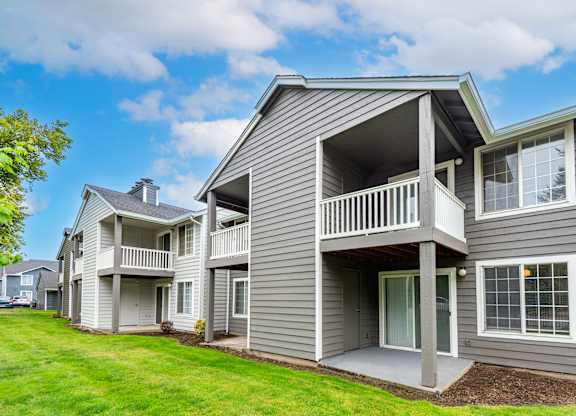 the view of a gray house with a balcony and a yard