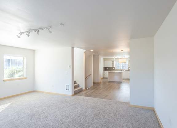 an empty living room with a kitchen in the background