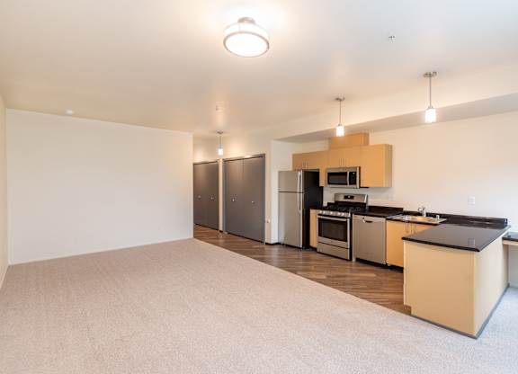 an empty living room with a kitchen with stainless steel appliances