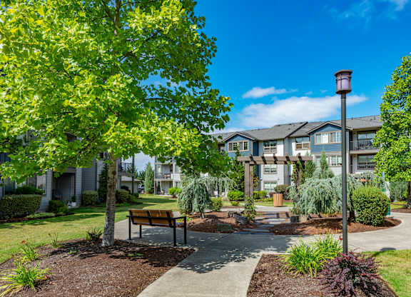 a park with trees and a bench in front of an apartment building