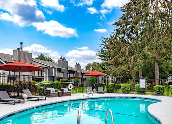 a swimming pool with umbrellas and chairs in front of apartment buildings