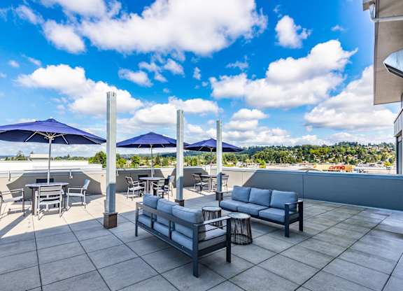 A patio with a table, chairs, and umbrellas overlooking a beach.