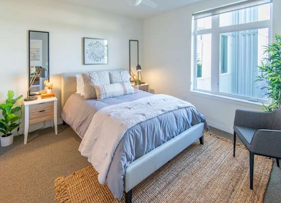 A bedroom with a large bed, a chair, and a potted plant.