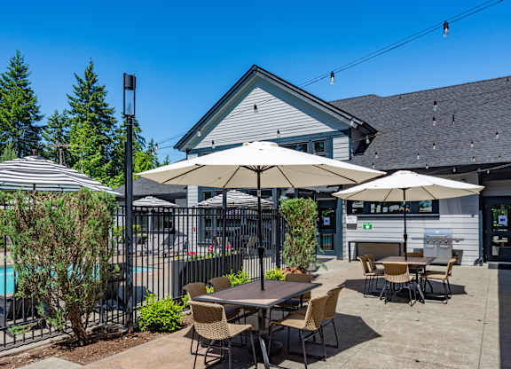 A poolside area with a table and chairs, umbrellas, and a building in the background.
