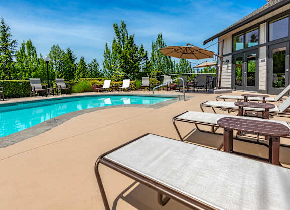 A poolside table is in front of a pool with chairs around it.