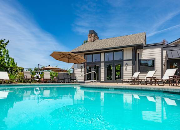 A large swimming pool in front of a house with a sun lounger.