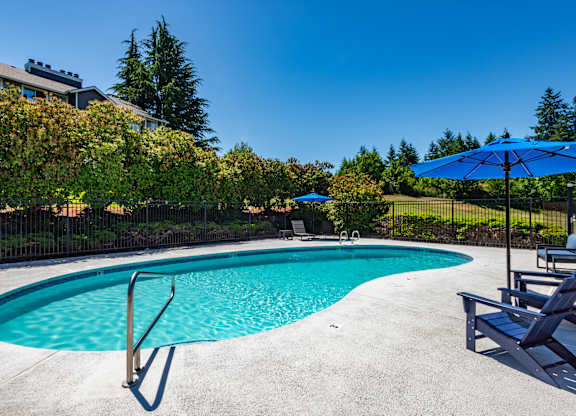 A swimming pool surrounded by trees and chairs with umbrellas.