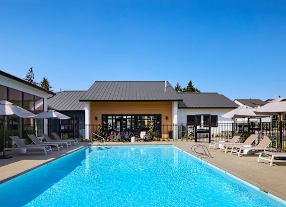 a swimming pool with lounge chairs and umbrellas in front of a building