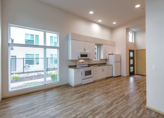 an empty living room with a kitchen and a large window