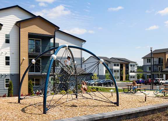 a playground with a climbing frame in front of a row of apartment buildings