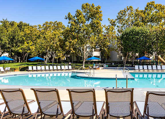 A pool surrounded by trees and chairs.