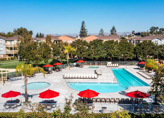 A pool surrounded by red umbrellas and chairs at The Woods Apartments, California