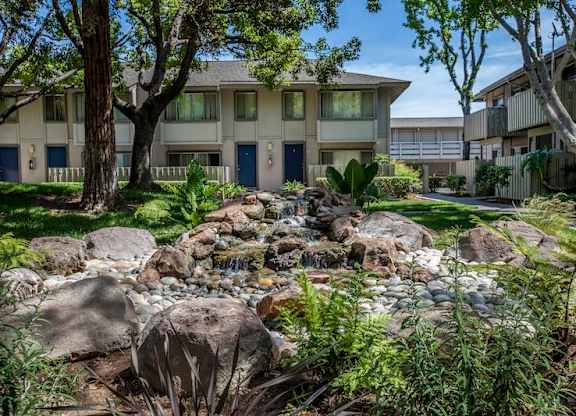 A stream of water flows through rocks in a garden at The Woods Apartments, San Jose, California