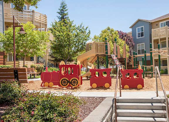 A playground with a red train and a slide at The Woods Apartments, California