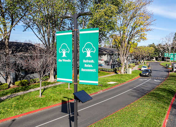 Two green signs with trees and the words at The Woods Apartments, San Jose, CA, 95136