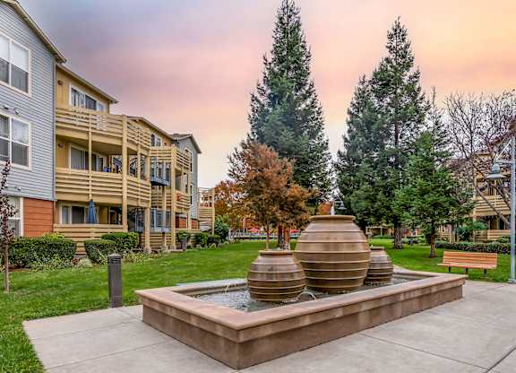 A courtyard with a fountain and apartment buildings in the background at The Woods Apartments, San Jose, 95136