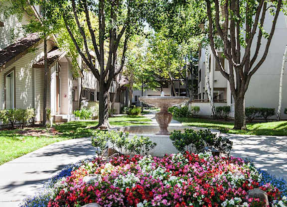 A garden with a variety of flowers in the foreground and a row of houses in the background at The Woods Apartments, California