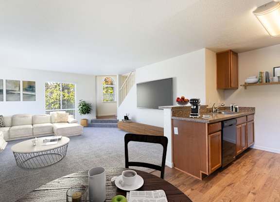 A modern living room with a white sofa, a wooden coffee table, and a kitchen area in the background at The Woods Apartments, San Jose