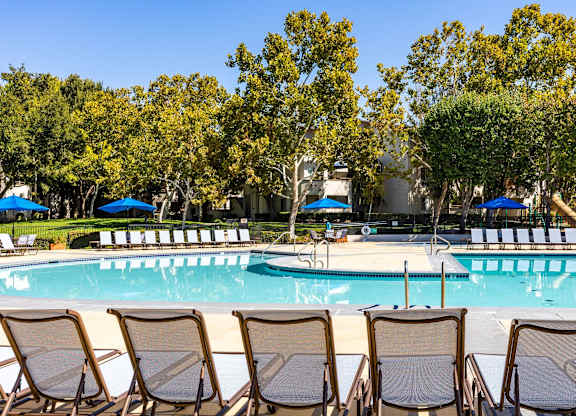 A pool surrounded by trees and chairs.
