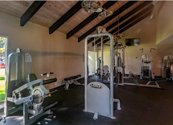 A gym with a variety of equipment including a weight machine and a rowing machine at Cherrywood Apartments, California