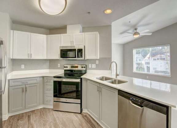 Modern Kitchen With Stainless Steel Appliance Suite, Spacious White Cabinetry, and Sleek Counters at Clock Tower Village, Washington, 98327