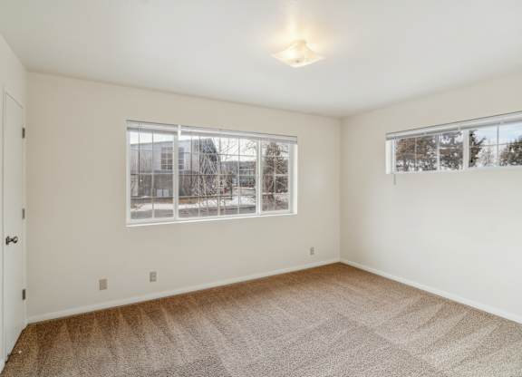 A room with a carpeted floor and two windows.