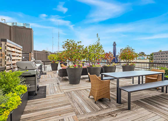 a rooftop patio with tables and chairs and plants and a grill