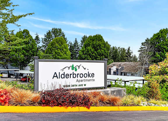 A sign for Alderbrooke Apartments is displayed in front of some trees.