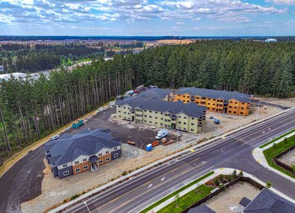 A large building complex is surrounded by a wooded area and a road.