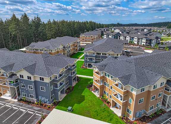 A large, multi-story residential building complex with a green lawn in the center.