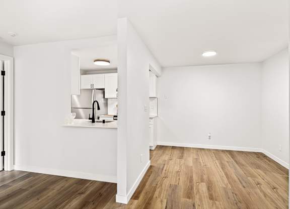 a living room and kitchen with white walls and wood floors
