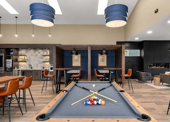 A pool table is in the middle of a room with a bar and chairs.