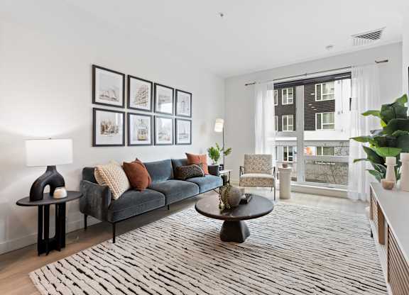 A living room with a grey couch, a coffee table, and a large window.