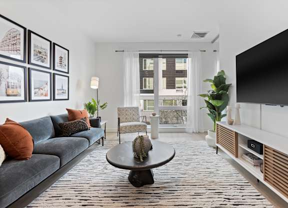 A living room with a grey couch, a black coffee table, and a large window with a view of a building outside.