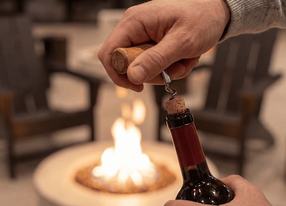A person is pouring wine into a bowl with a fire in the background.