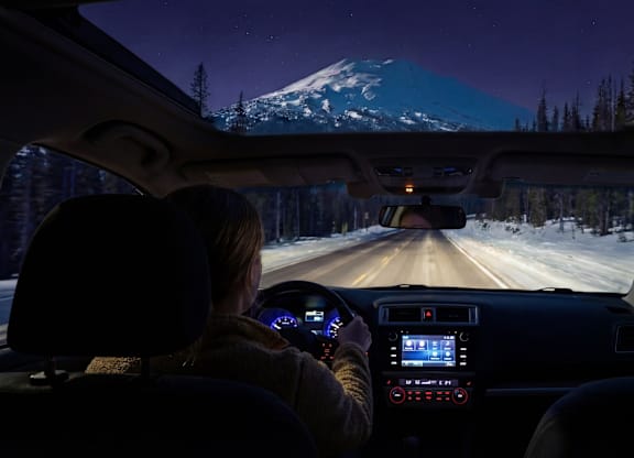 A person is driving a car at night with a view of a snowy mountain in the background.