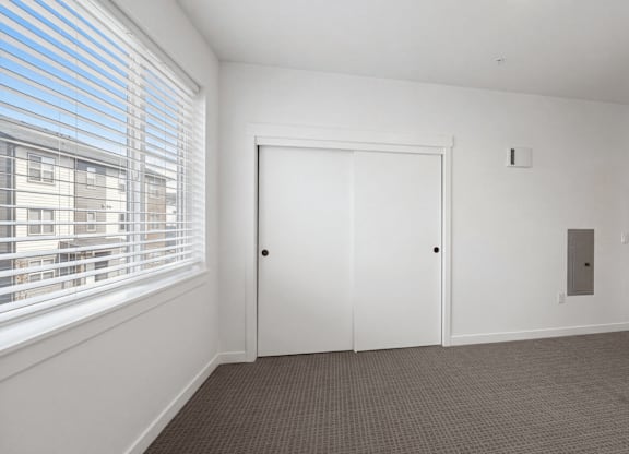 A room with a white door, carpeted floor, and a window with blinds.