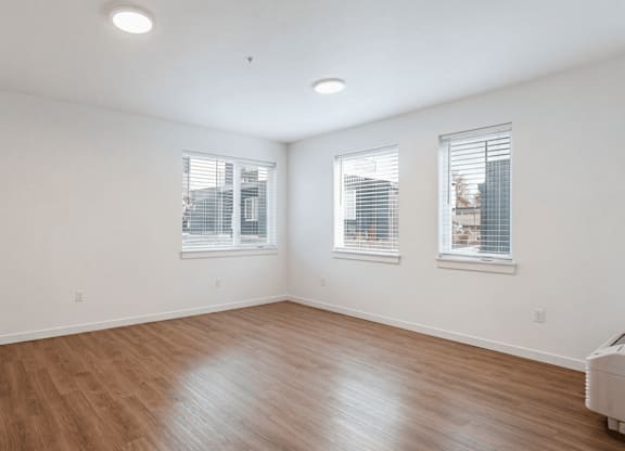 A room with wooden flooring and two windows.
