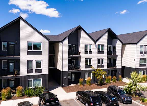 A modern apartment complex with black and white buildings and cars parked in the driveway.