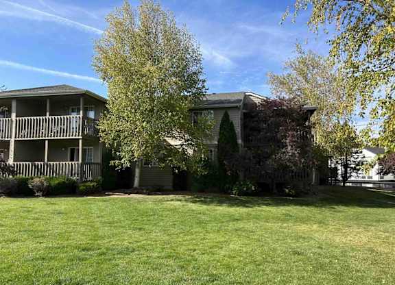 A grassy area in front of a two-story house with a tree in the foreground.